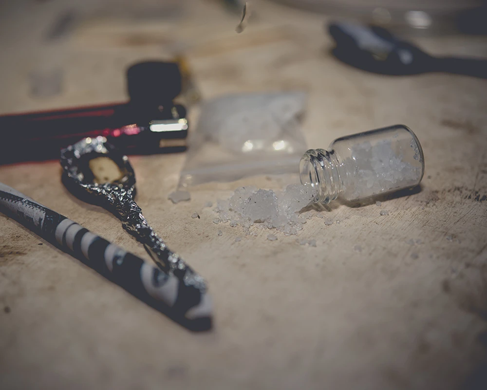 Kristalachtige flakka ligt op tafel naast attributen voor drugsgebruik. De afbeelding laat middelengebruik en de risico’s van flakka zien.