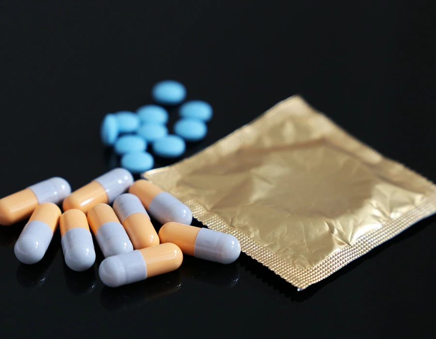 Capsules, blauwe pillen en een condoomverpakking, ter illustratie van chemsex.