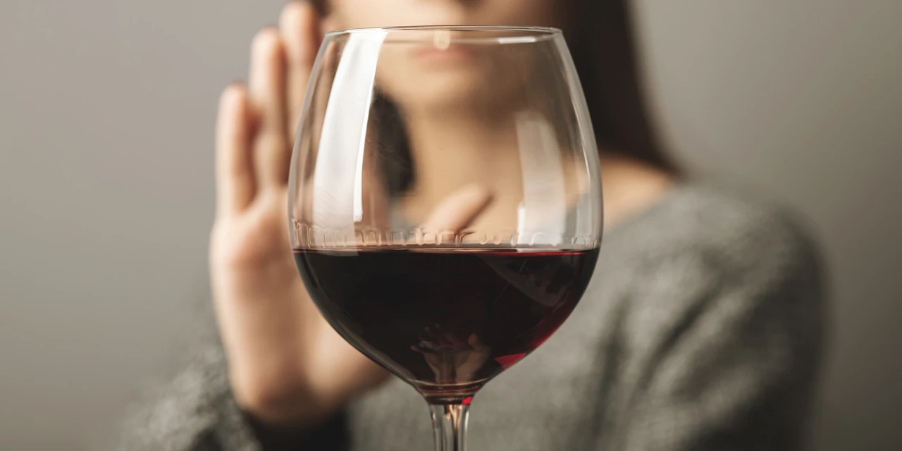 Een vrouw houdt haar hand omhoog om een glas rode wijn af te wijzen tijdens een moment van bewust kiezen voor minder alcohol.