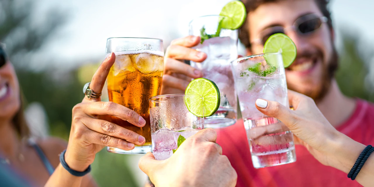 Een groep vrienden proost met alcoholische drankjes tijdens een sociale bijeenkomst in de buitenlucht.
