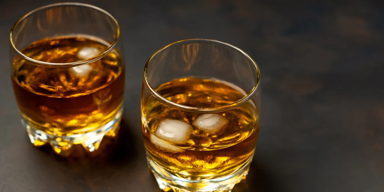 Twee glazen met sterke drank en ijsblokjes staan op een donkere tafel.