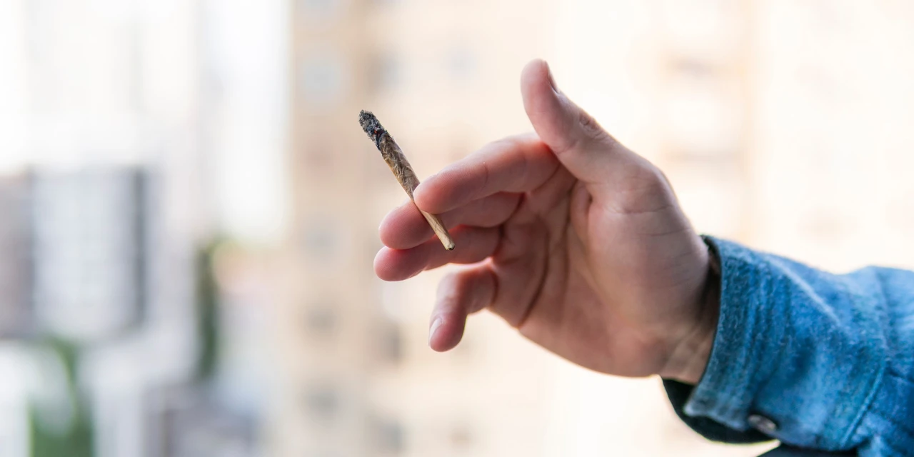 Een hand houdt een brandende joint vast met een wazige achtergrond op de achtergrond.
