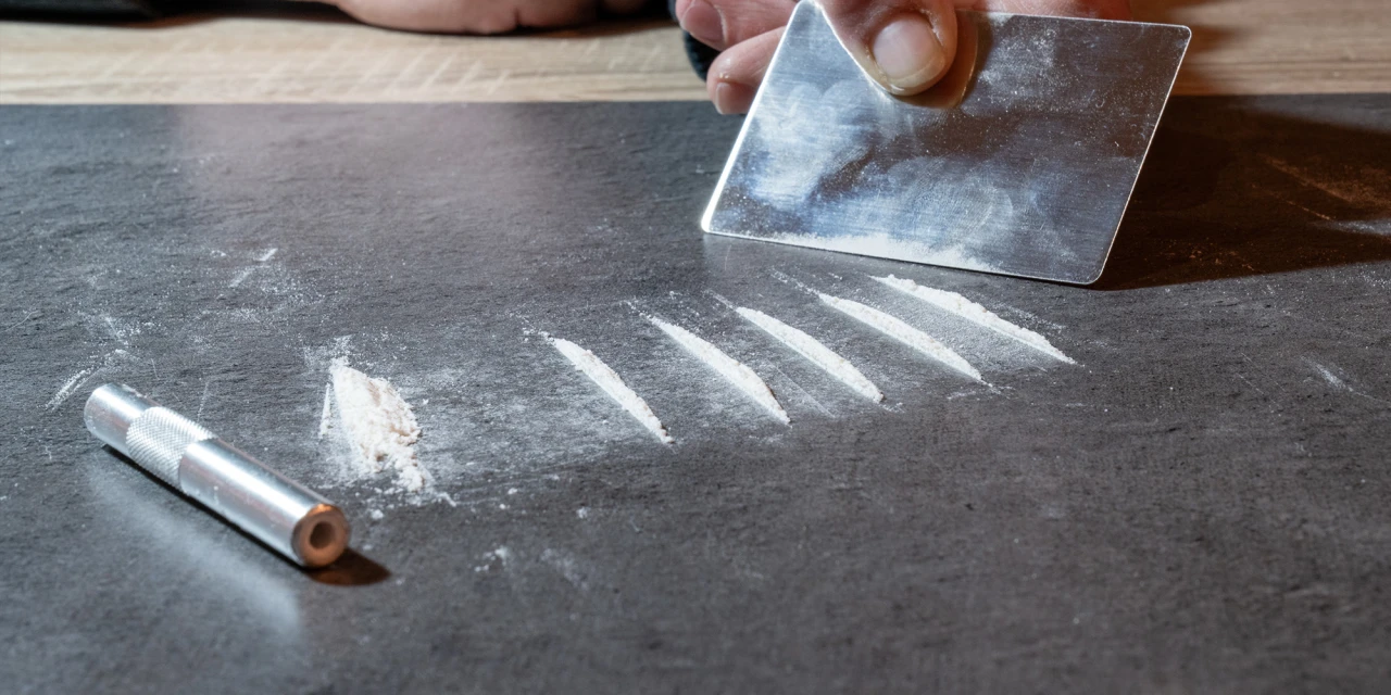 Persoon verdeelt lijnen cocaïne op tafel met een pasje, passend bij cocaïnegebruik en cocaïneverslaving.