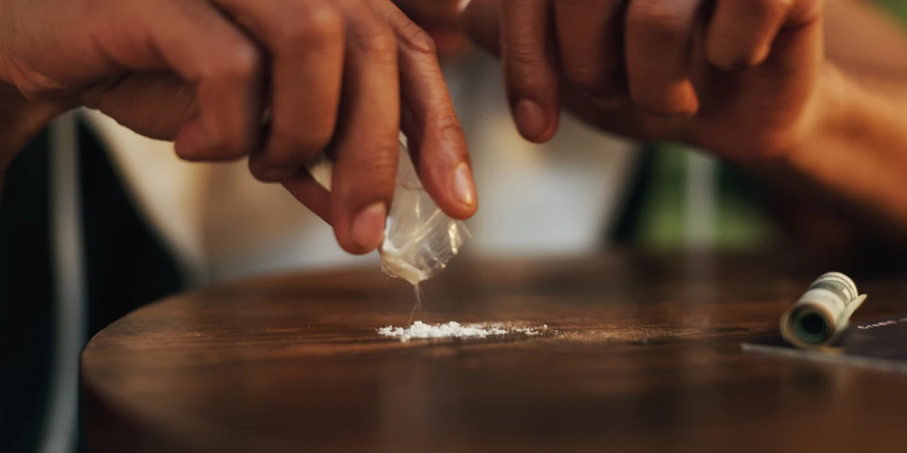 Persoon strooit cocaïne uit een zakje op tafel, passend bij cocaïnegebruik en afkickverschijnselen van coke.