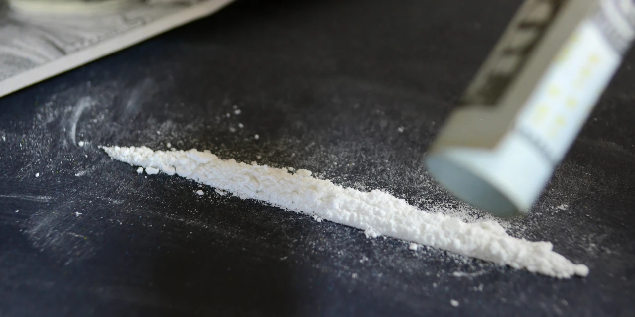 Lijn cocaïne op een donkere tafel met opgerold briefje op de achtergrond, passend bij cocaïnegebruik en verslavingssignalen.