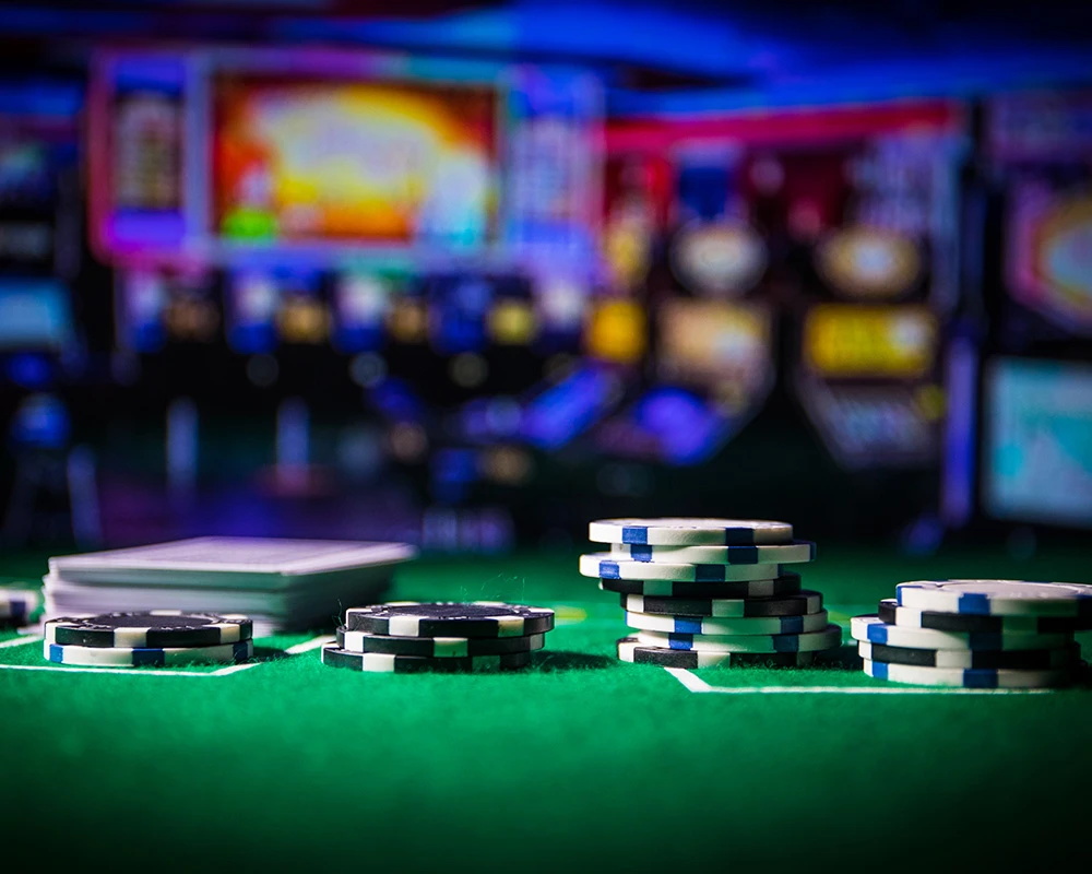 Fiches en speelkaarten liggen op een goktafel met casinolichten op de achtergrond. De afbeelding verwijst naar gokken en situaties waarin hulp bij gokverslaving nodig kan zijn.