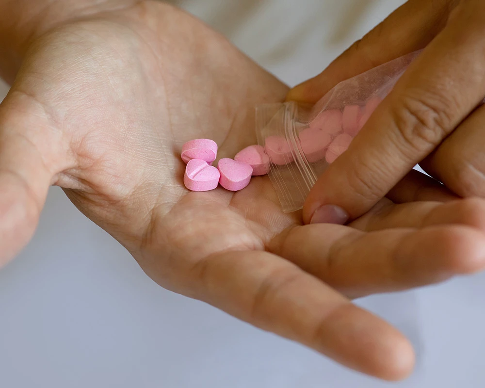 Roze MDMA pillen worden uit een zakje in een hand gegoten. De afbeelding laat recreatief drugsgebruik zien en past bij informatie over MDMA effecten.