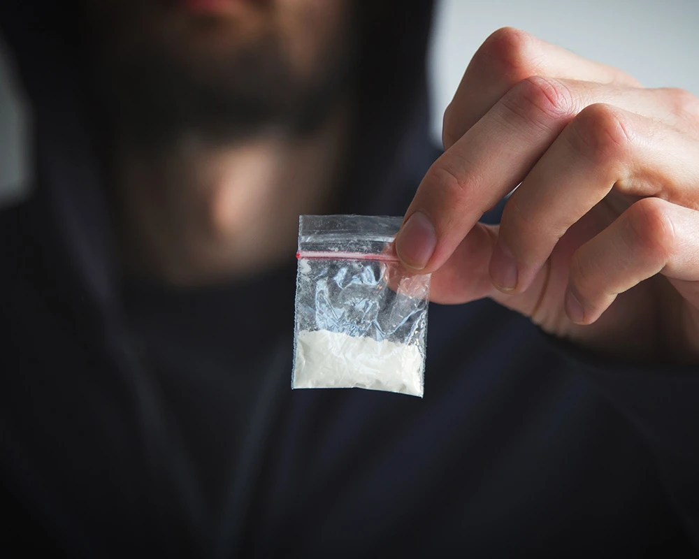 Persoon houdt een klein zakje met witte drugs vast. De afbeelding past bij informatie over speedgebruik herkennen en signalen van speedgebruik.