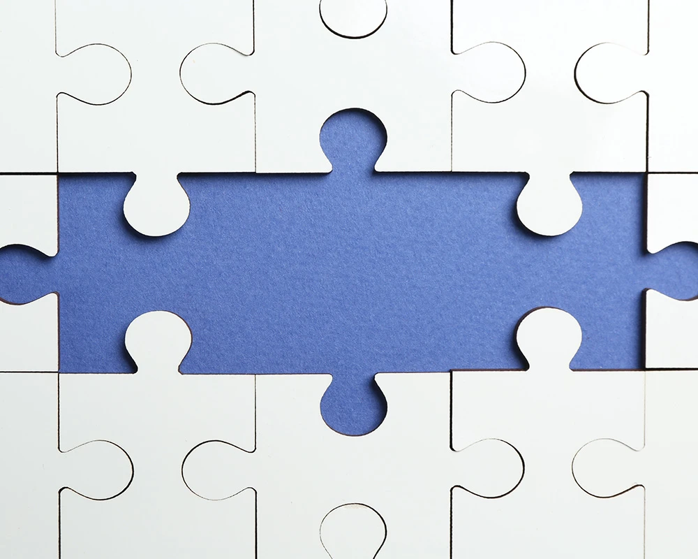 Witte puzzelstukken met een ontbrekend middenstuk als symbool voor mentale gezondheid, autisme en verslavingsproblematiek. De afbeelding past bij informatie over verslaving en autisme.