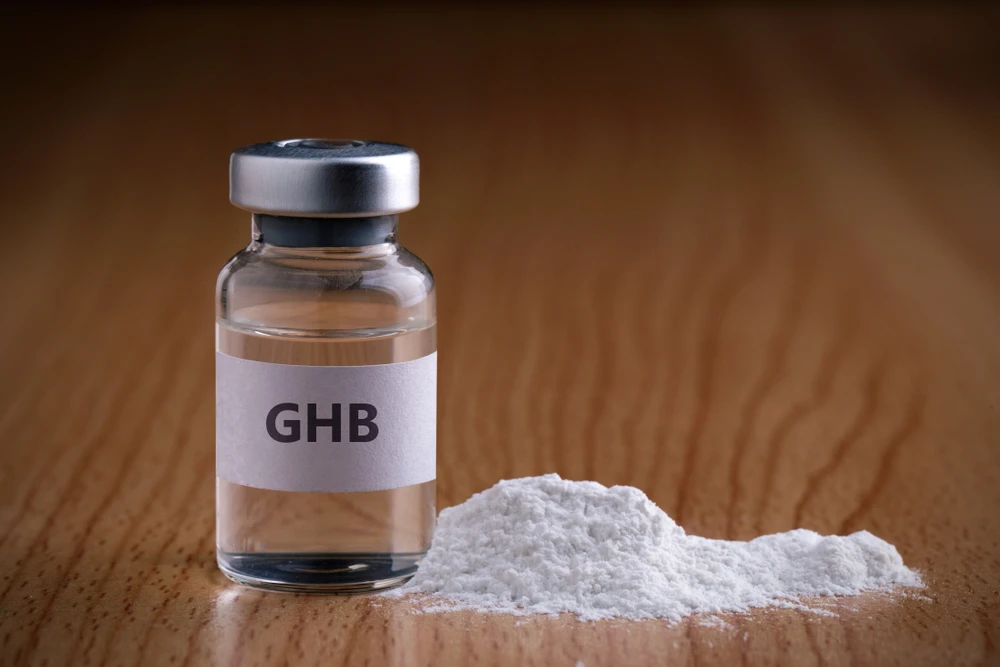GHB-flesje en wit poeder op tafel, illustratie van GHB-verslaving.