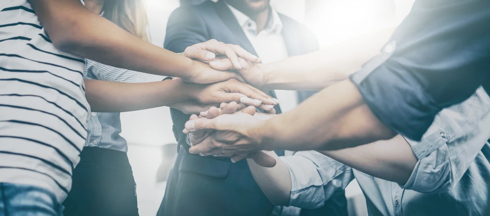 handen-op-elkaar-als-team Groep mensen die handen op elkaar leggen als team.