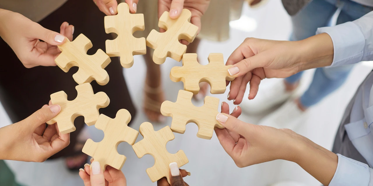 Mensen brengen puzzelstukken samen als symbool voor samenwerking en herstel binnen verslavingszorg.