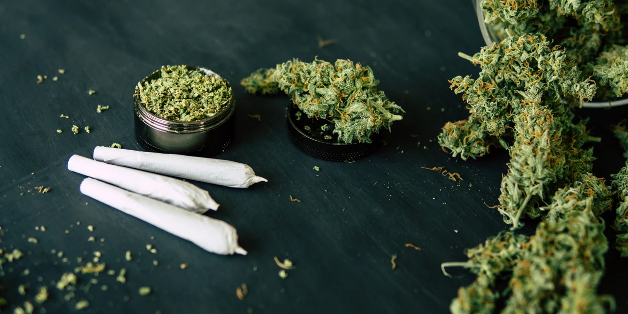Joints, gemalen cannabis en wiettoppen liggen verspreid op een donkere tafel.