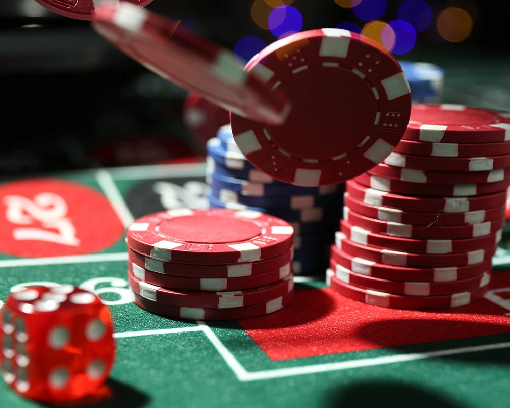 Rode fiches en dobbelstenen liggen op een speeltafel in een casinoomgeving. De afbeelding verwijst naar kansspelen en gokken in het casino.