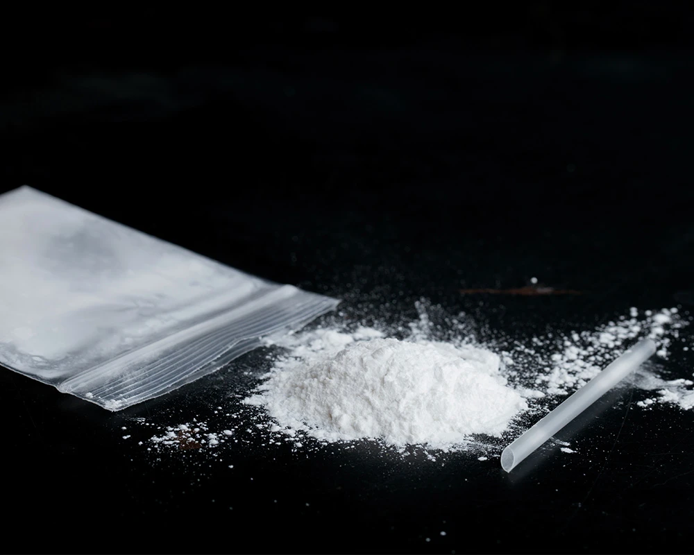 Zakje met wit poeder en een rietje naast ketamine op een donkere tafel. De afbeelding sluit aan bij informatie over wat is ketamine en recreatief drugsgebruik.