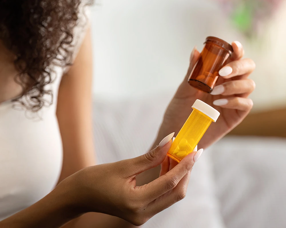 Vrouw bekijkt verschillende medicijnpotjes met medicatie in haar handen. De afbeelding verwijst naar medicijngebruik en de mogelijke risico’s van een medicijnverslaving.