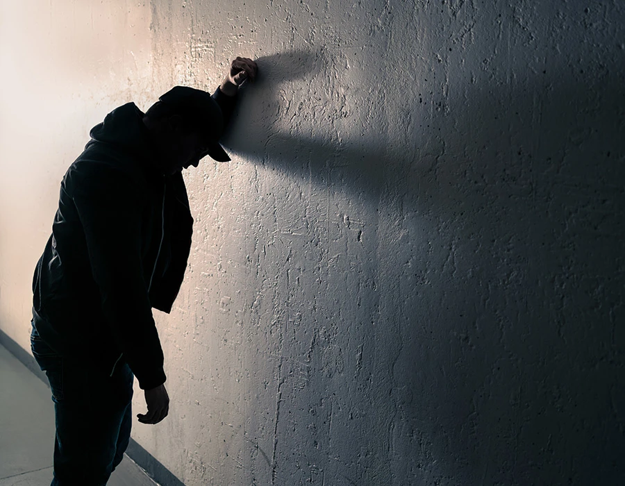 Persoon leunt uitgeput tegen een muur en oogt somber.