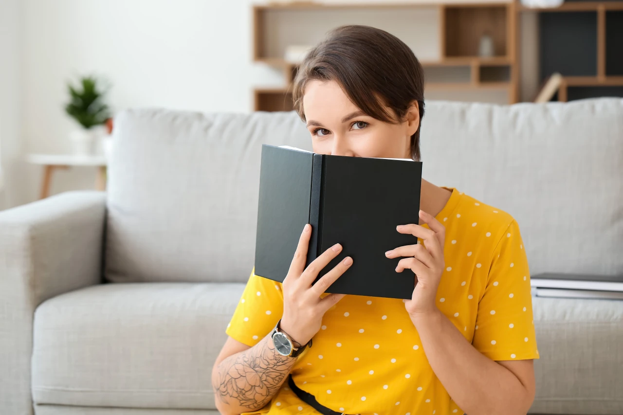 vrouw-verbergt-gezicht-half-achter-boek Vrouw in gele blouse verbergt gezicht half achter notitieblok zodat haar privacy gewaarborgd blijft.