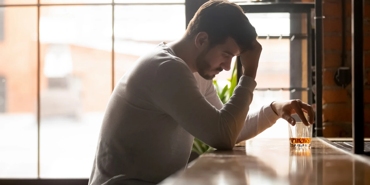 Een man zit alleen aan een bar met een glas alcohol en kijkt somber tijdens een periode van alcoholproblemen of ontwenning.