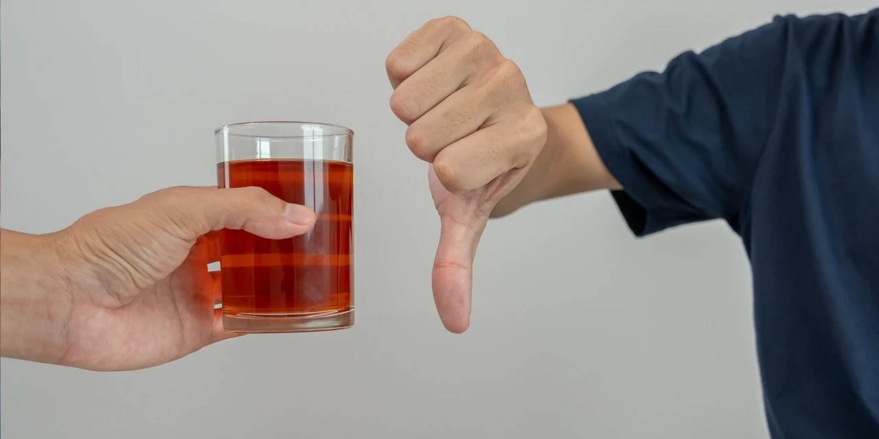 Een persoon geeft een duim omlaag naast een glas alcohol om afwijzing van alcoholgebruik te laten zien.