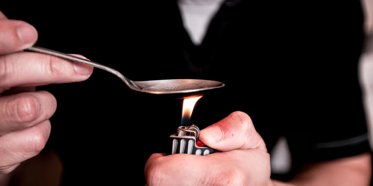 Persoon verhit cocaïne op een lepel met een aansteker, passend bij cocaïne roken en crackgebruik.
