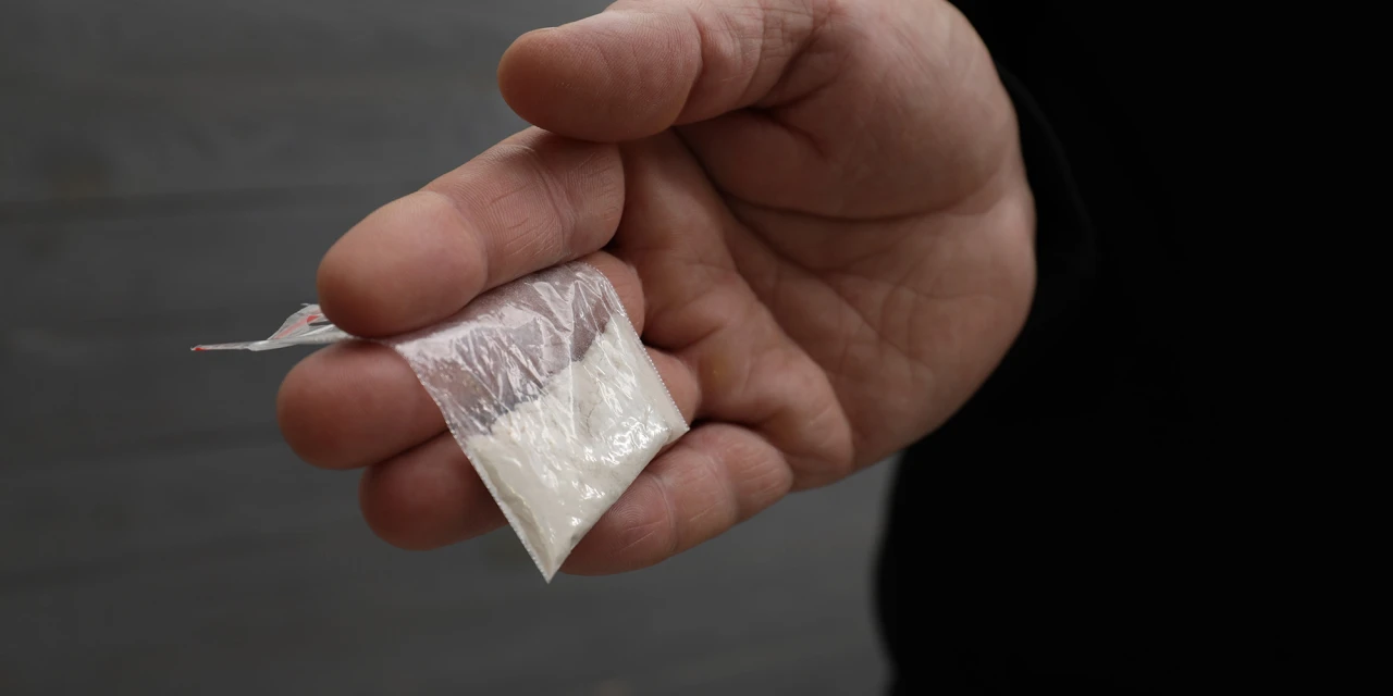 Persoon houdt een klein zakje met cocaïne vast in de hand, passend bij uitleg over wat coke is.
