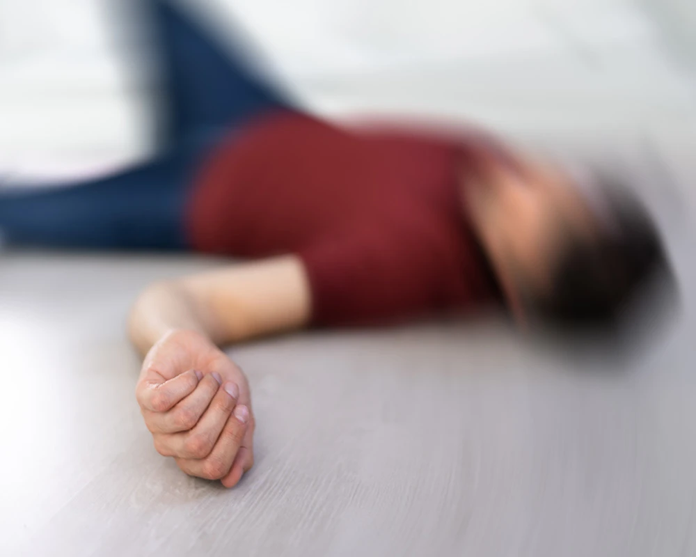 Een persoon ligt bewusteloos op de vloer terwijl de arm op de voorgrond zichtbaar is. De afbeelding laat een ernstige situatie zien die kan passen bij out gaan door middelengebruik.