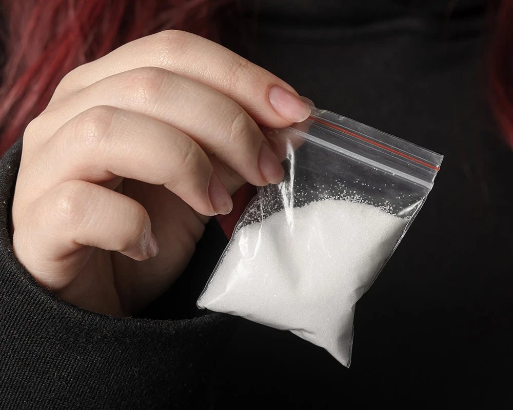Persoon houdt een klein zakje met wit poeder vast dat verwijst naar ketaminegebruik. De afbeelding past bij de uitdagingen rondom stoppen met ketamine en afhankelijkheid.