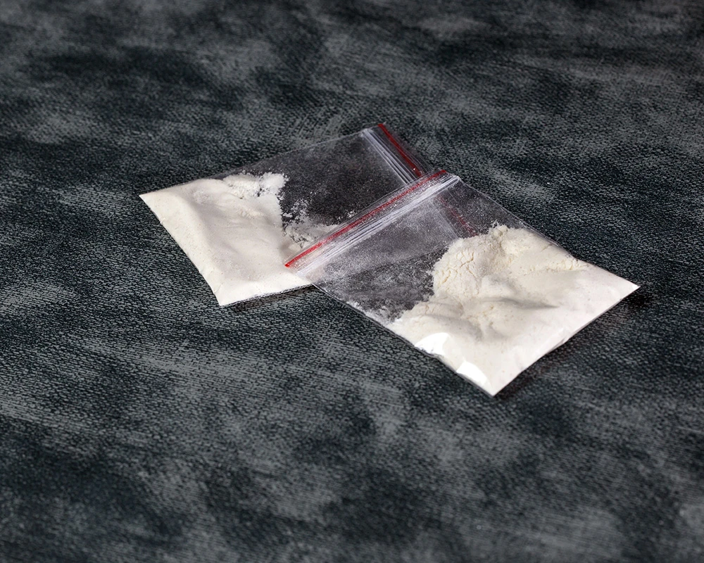 Twee kleine zakjes met wit speedpoeder liggen op een donkere ondergrond. De afbeelding verwijst naar drugsgebruik en een mogelijke speedverslaving.