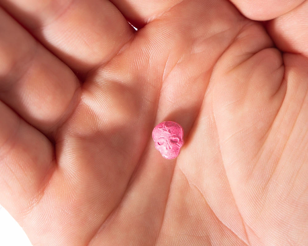 Roze XTC-pil in schedelvorm ligt in een open hand. De afbeelding past bij informatie over XTC verslaving en de risico’s van XTC-gebruik.