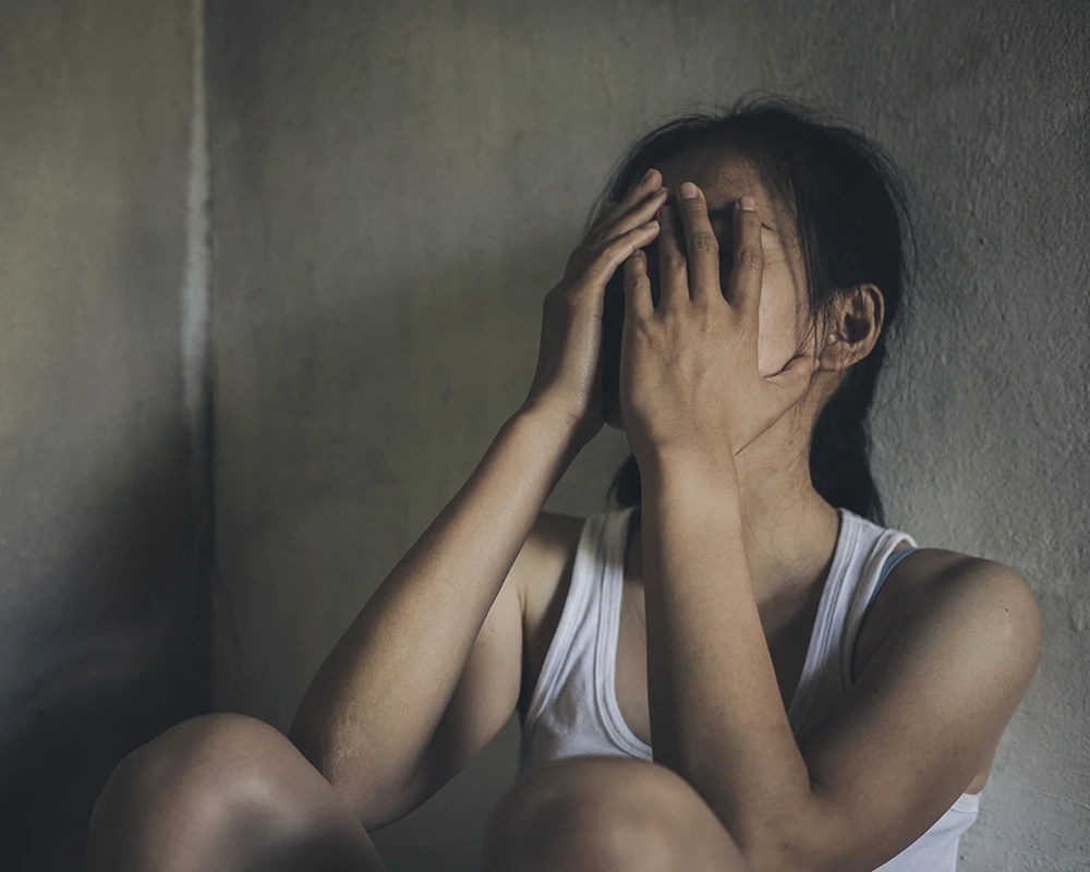 Vrouw zit verdrietig tegen een muur met haar handen voor haar gezicht. De afbeelding past bij informatie over ontwenningsverschijnselen en emotionele klachten tijdens het afkicken.