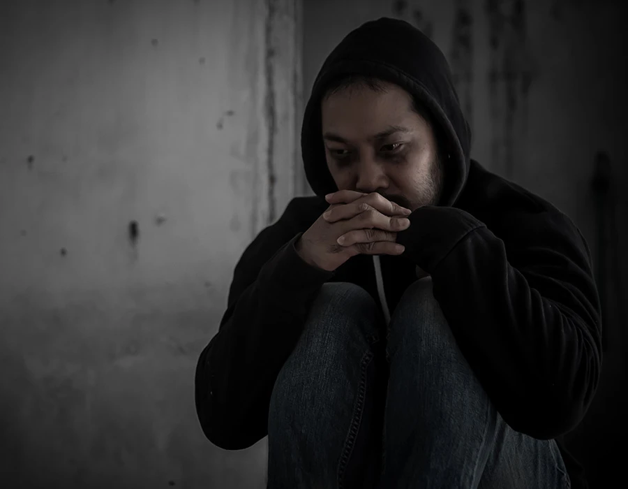 Sombere persoon in hoodie zit alleen in een donkere ruimte. De afbeelding hoort bij de mentale en emotionele gevolgen van cross addiction en verslavingsproblematiek.