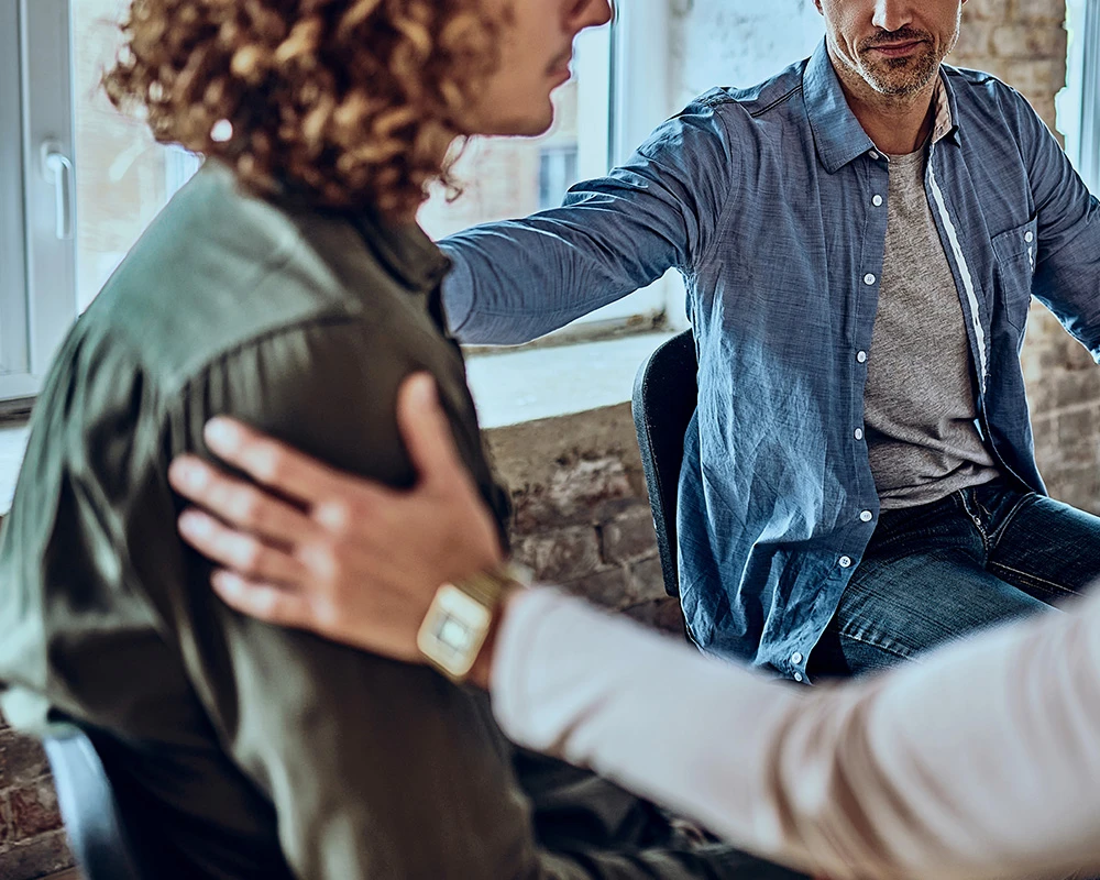 Een behandelaar en betrokkenen bieden steun tijdens een gesprek over herstel en verslavingszorg in een rustige behandelomgeving.