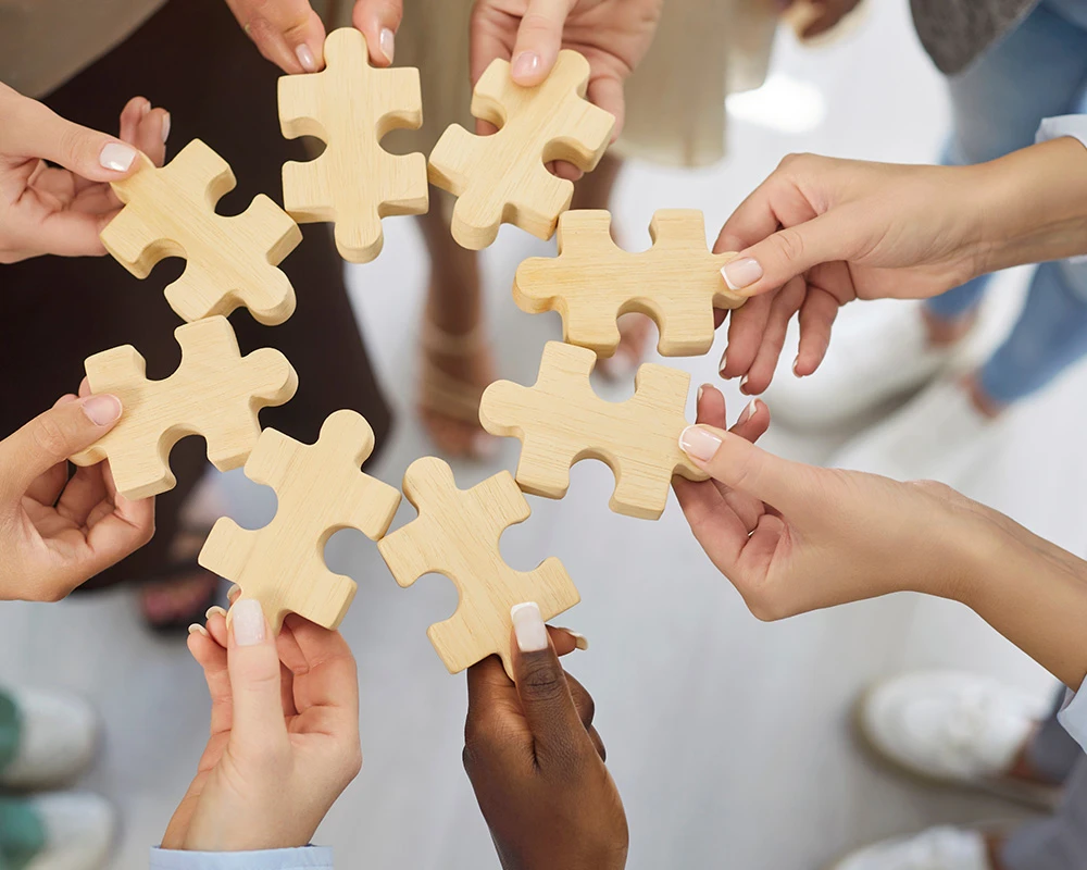 Meerdere mensen houden puzzelstukken vast als symbool voor samenwerking, ondersteuning en persoonlijke begeleiding binnen de verslavingszorg.