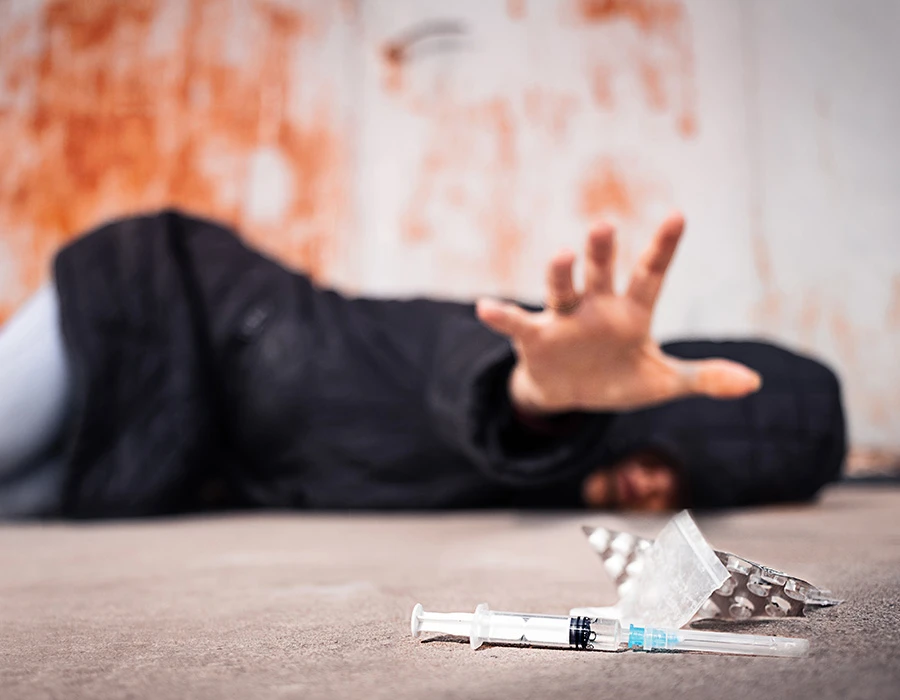Persoon op de grond naast een injectiespuit en drugs.