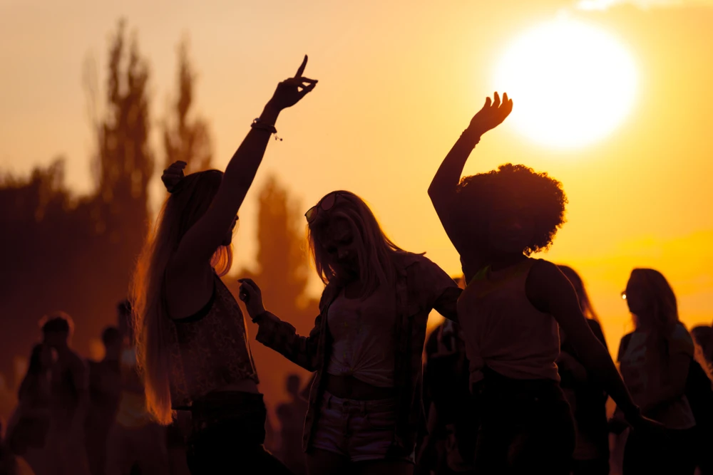3 vrouwen dansen op festival met veel mensen die mogelijk symptomen vertonen van te veel alcohol. 