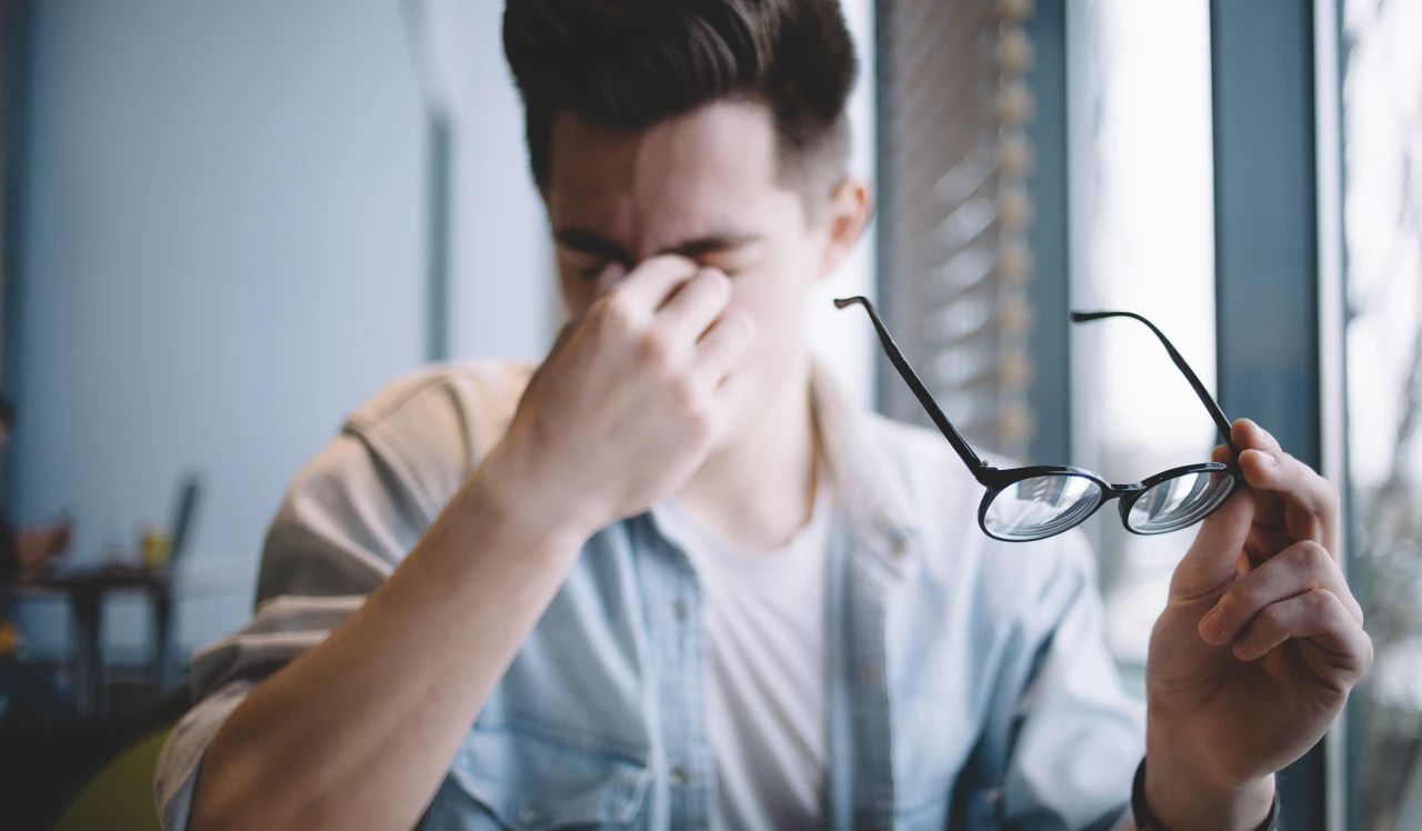 man-zet-bril-af-en-is-vermoeid Man doet bril af omdat hij last heeft van de afkickverschijnselen van wiet.