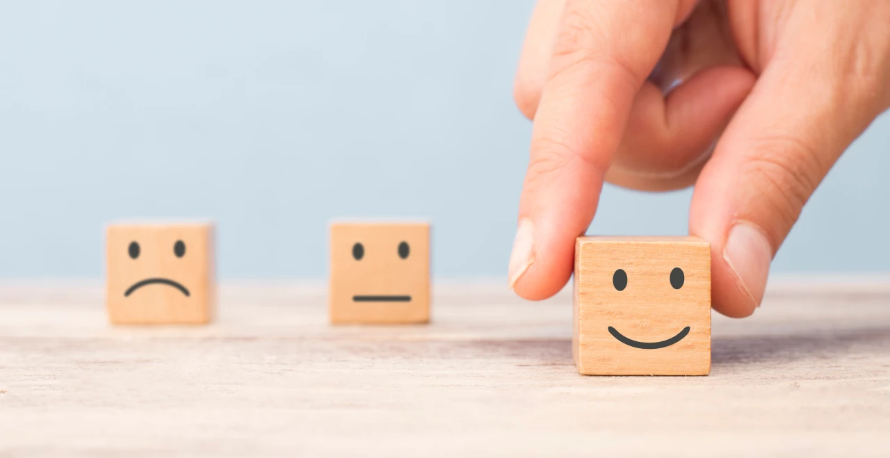 blokjes-met-gezichtje-erop-en-hand-die-1-blokje-pakt Houten blokjes met sip, neutraal en blij gezicht, die klachten en complimenten uitbeelden.